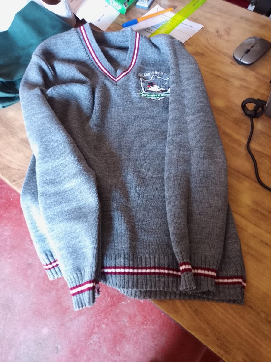 School crest embroidered on a grey v-neck school sweater with striped trim, Kenya